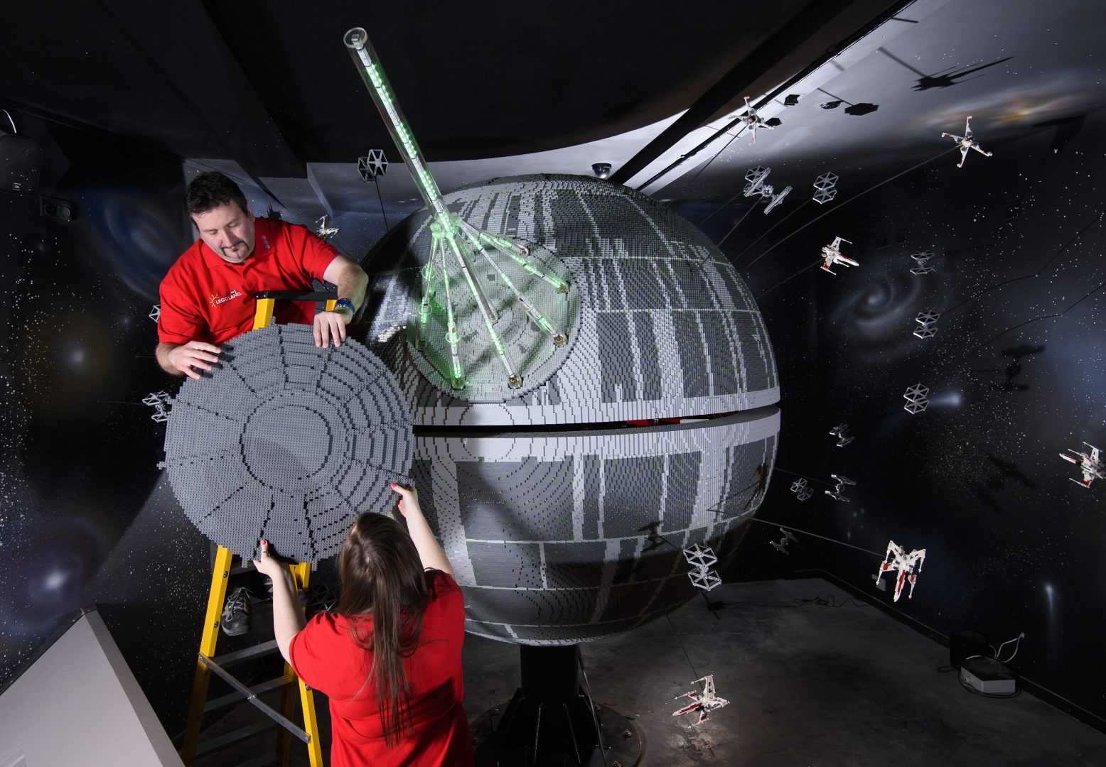 SHOT 13. Caption. ONE OF THE WORLD’S BIGGEST EVER LEGO® STAR WARS™ MODELS INSTALLED AT THE LEGOLAND® WINDSOR RESORT.   LAST PIECES PUT IN PLACE ON 500,000 LEGO® BRICK DEATH STAR LEGOLAND® Model Makers Giorgio Pastero and Phoebe Rumbol lift the top piece into place, onto one of the biggest and most impressive LEGO® Star Wars™ models ever created - a 500,000 brick LEGO® Star Wars™ recreation of The Death Star. The operation took three days as the massive new 2.4 metre wide, 3 metre high creation was carefully hoisted into position and the final bricks were put in place. The hefty 860kg perfectly spherical model took 15 Model Makers three months to build and will be the centrepiece of an epic new finale at the LEGO®Star Wars™ Miniland Model Display when the Resort opens on 11 March and guests will be able to trigger special effects and bright the scene to life. TM & © Lucasfilm Ltd. All rights reserved